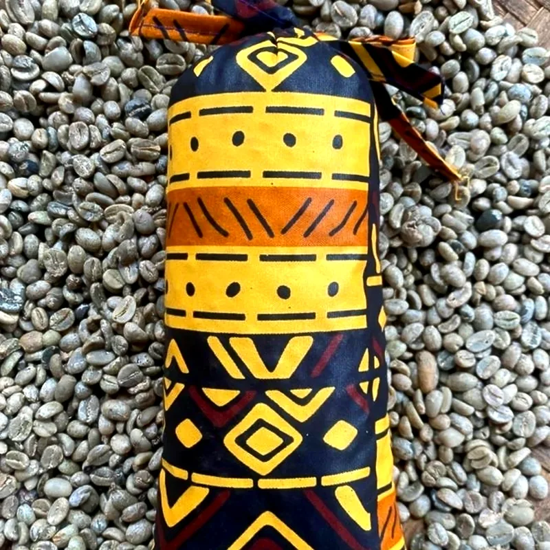 A yellow and black mud-cloth pouch on a bed of pale green unroasted coffee beans