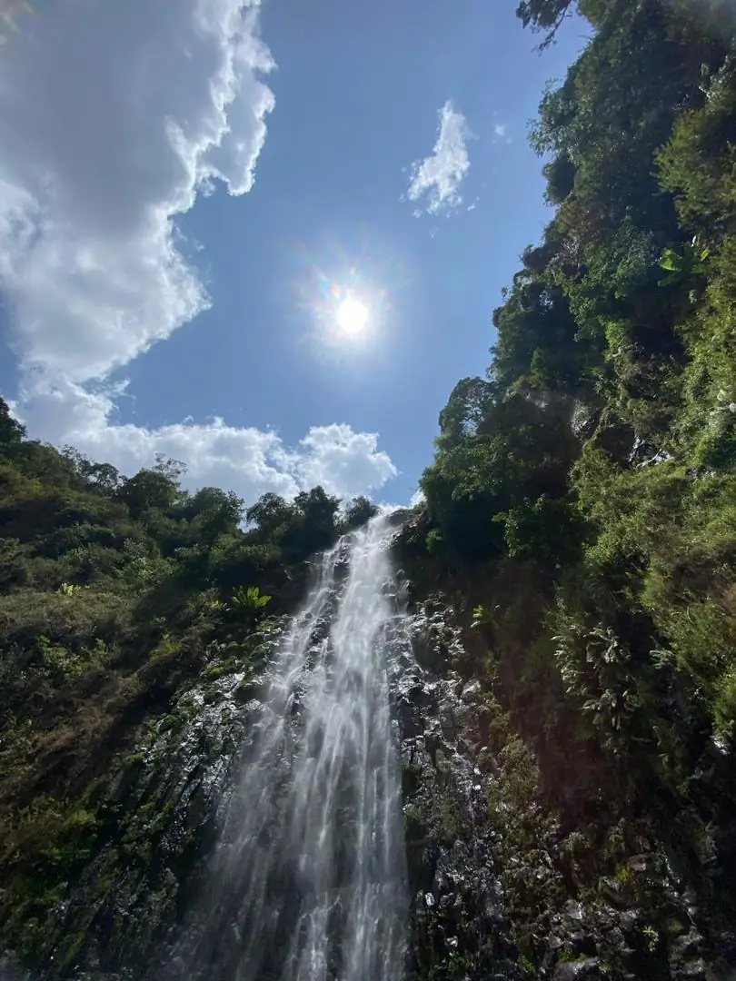 Materuni Falls seen from below with the sun bursting over the green cliff edge