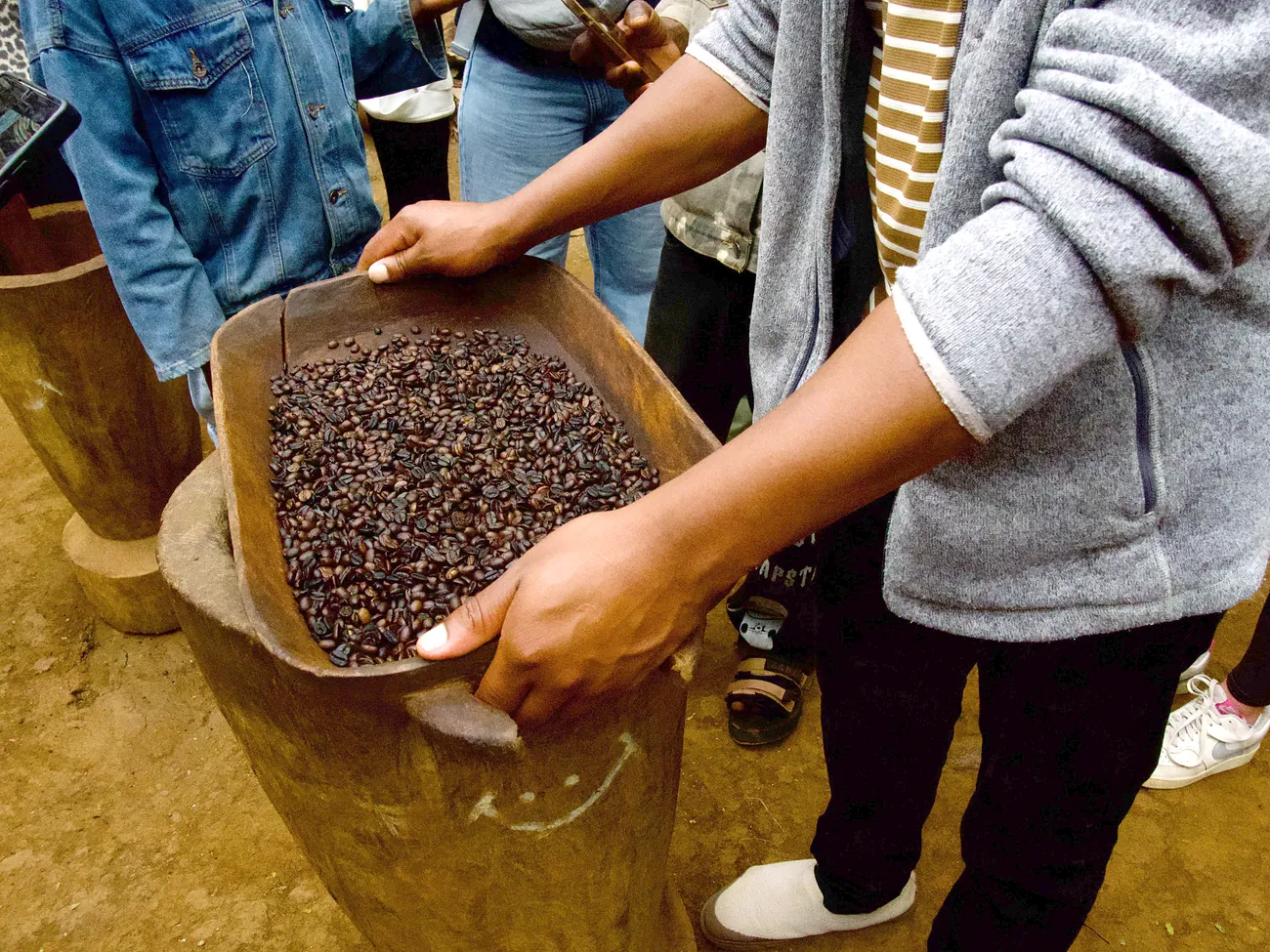 A wooden tray of dark roasted Materuni arabica held out over the mortar