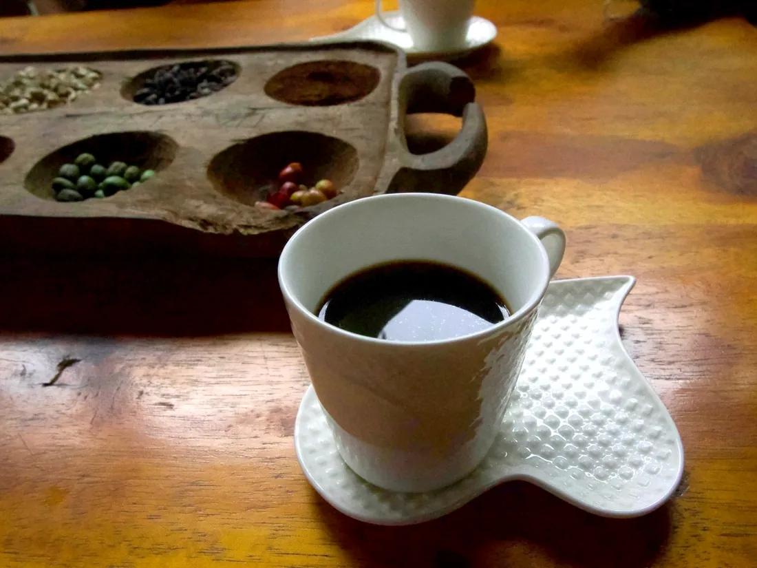 A finished cup of Materuni coffee beside the carved tray of cherries, green beans and roasted beans